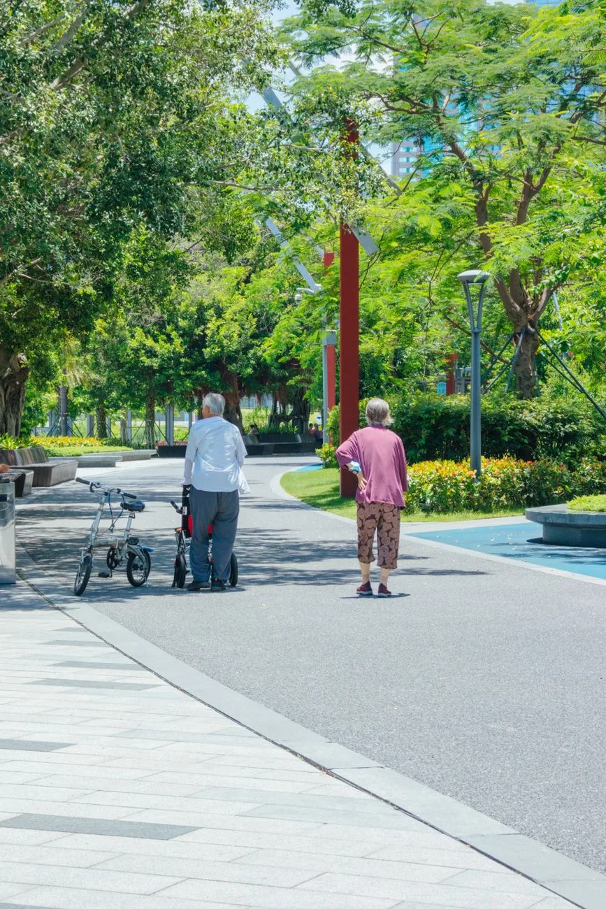 Two senior adults walking in a sunlit, green park enjoying leisure time and nature.